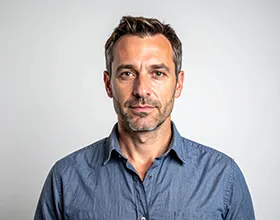 Portret muškarca srednjih godina u plavoj košulji, koji ozbiljno gleda u kameru, na svijetloj pozadini.